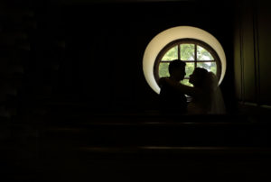 Bride and groom are silhouetted in a window in the Wren Chapel in Williamsburg, Virginia